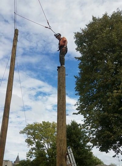 man standing on a tall wooden pole