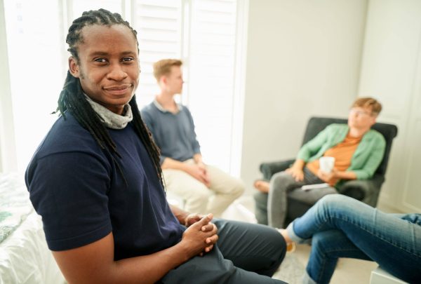 African man sitting at a mental health session looking at camera with people sitting at back